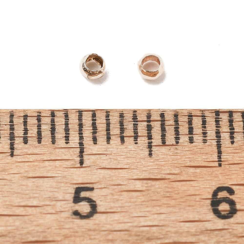 Rose gold round crimp beads 2mm warm blush rose gold plating open barrel shown bulk scattered close-up and ruler scale jewellery making Australia